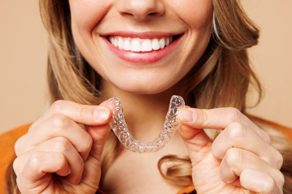 Smiling woman holding clear Invisalign aligners in Lowell, MA