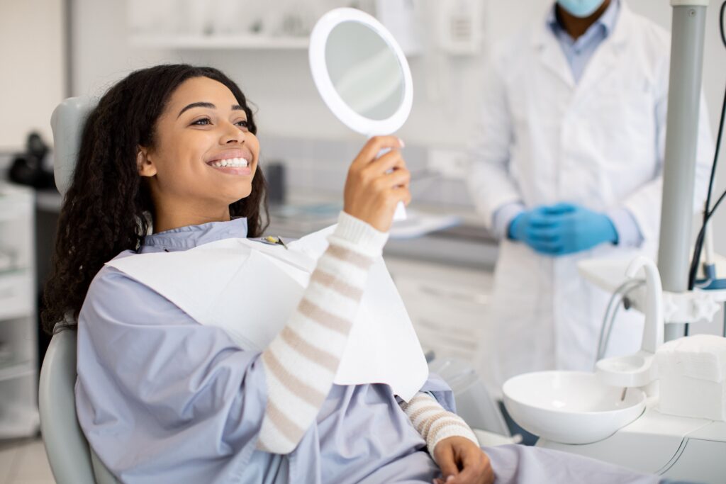 Woman checking her smile in a mirror after a fluoride treatment at All Smile Care