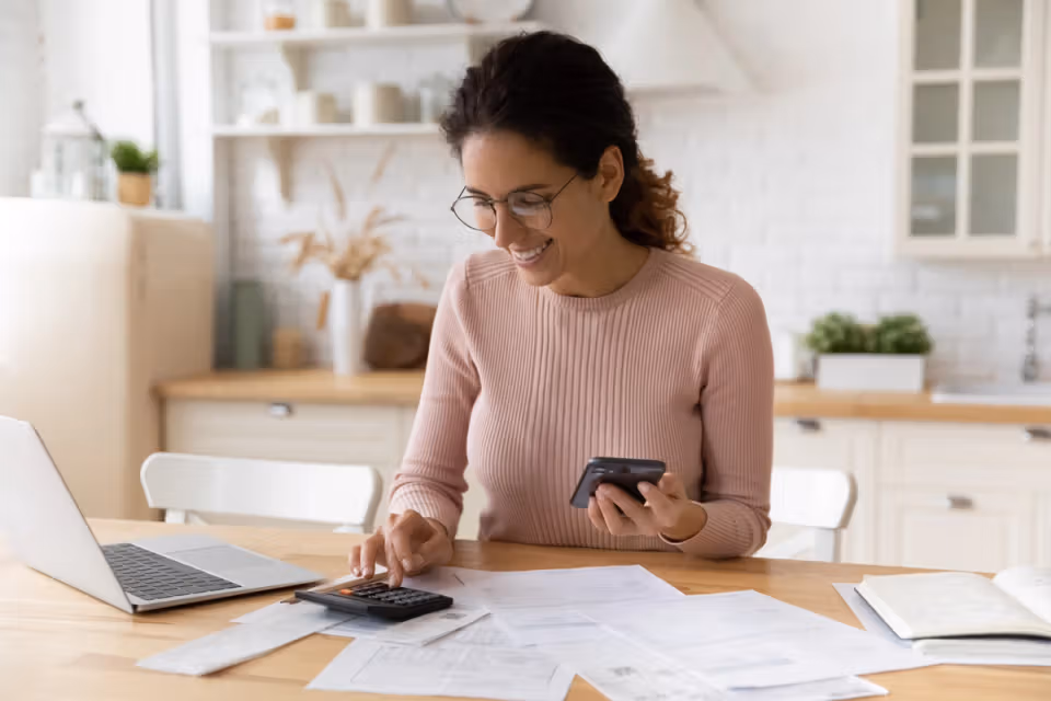 Woman using a calculator and phone while reviewing bills at home
