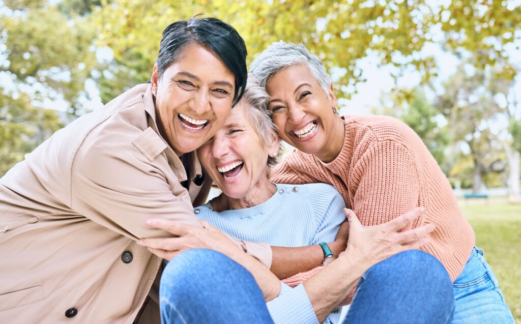 Three women laughing together after restoring their smiles with implant-supported bridges