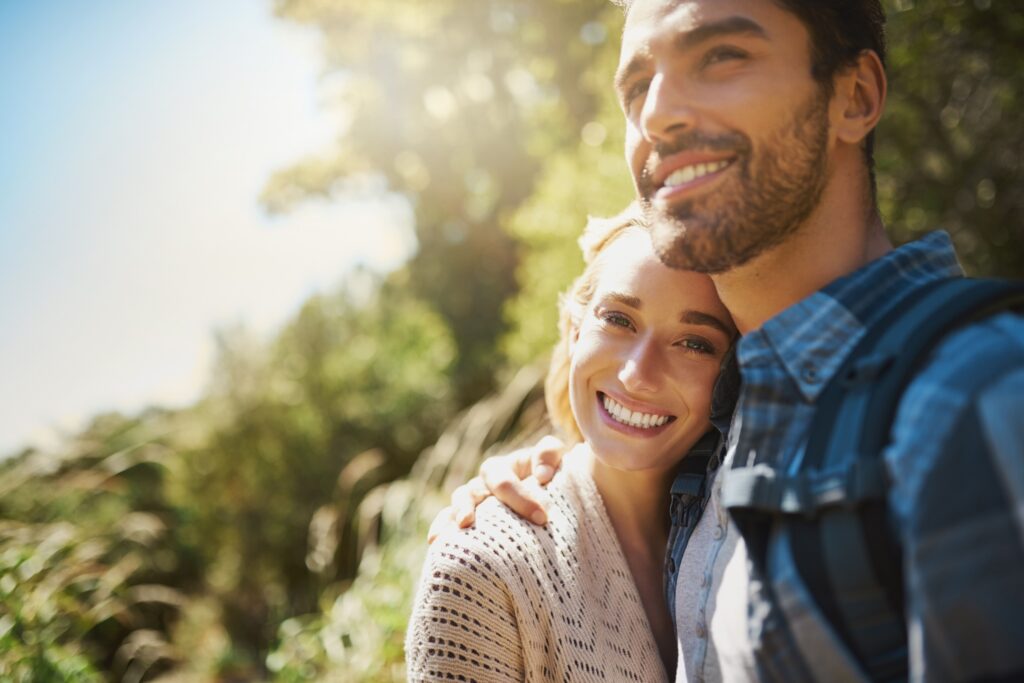 Smiling couple embracing outdoors after cosmetic dentistry treatment at All Smile Care