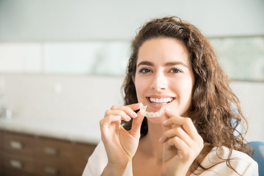 Smiling woman holding an Invisalign clear aligner at All Smile Care
