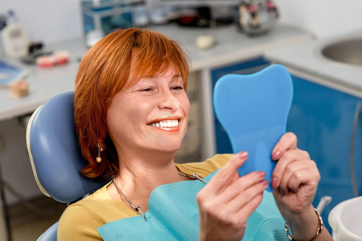 Dental patient smiling at her reflection after treatment