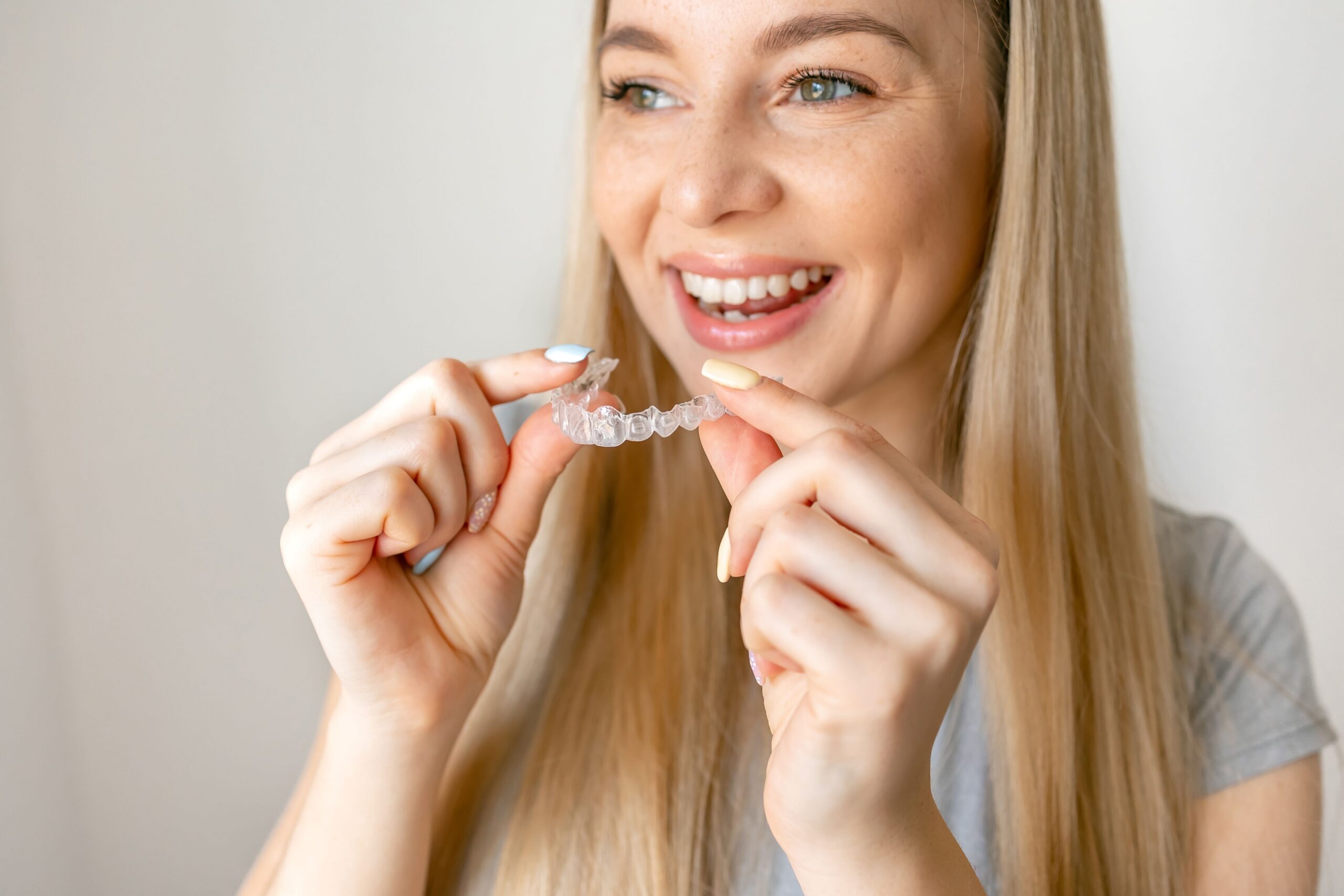 Smiling woman holding a clear Invisalign aligner
