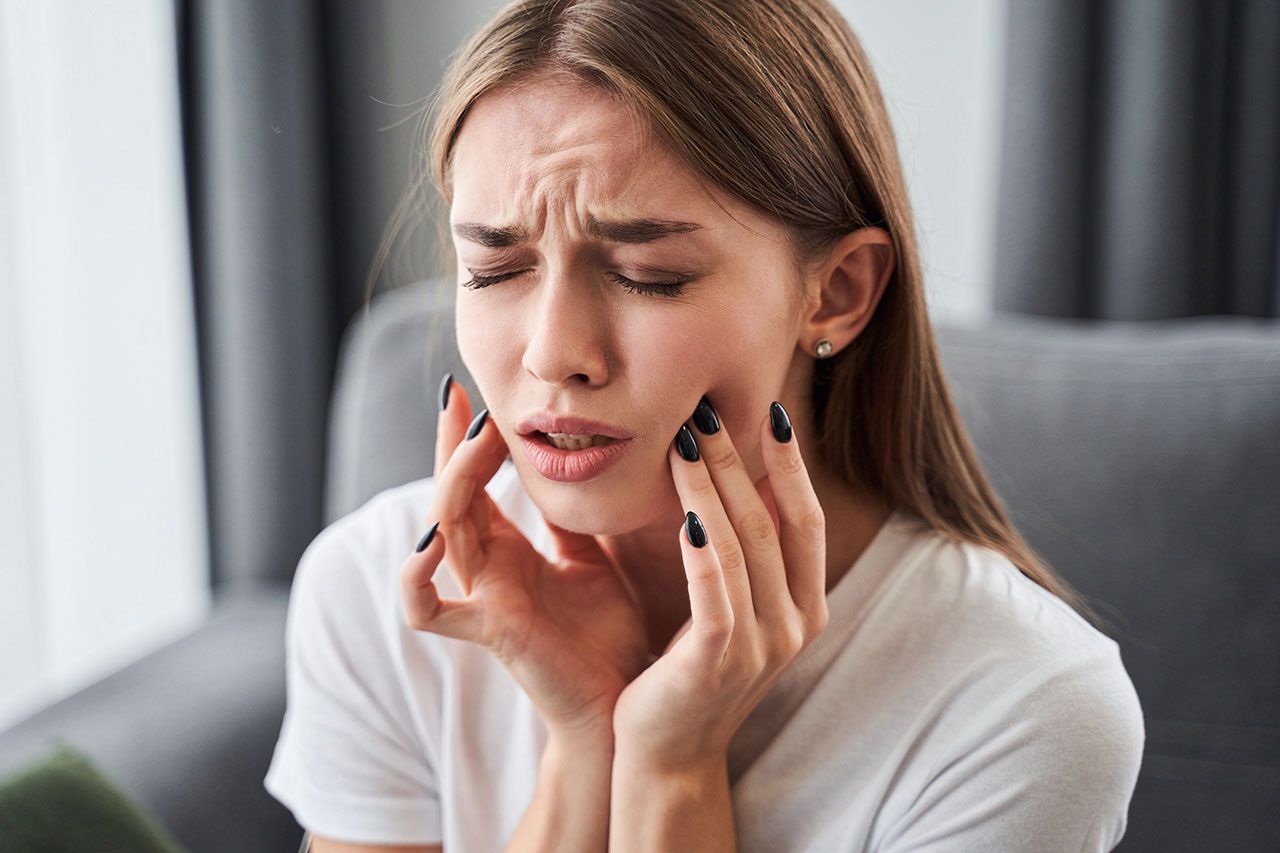 Woman holding her cheeks in pain, eyes closed